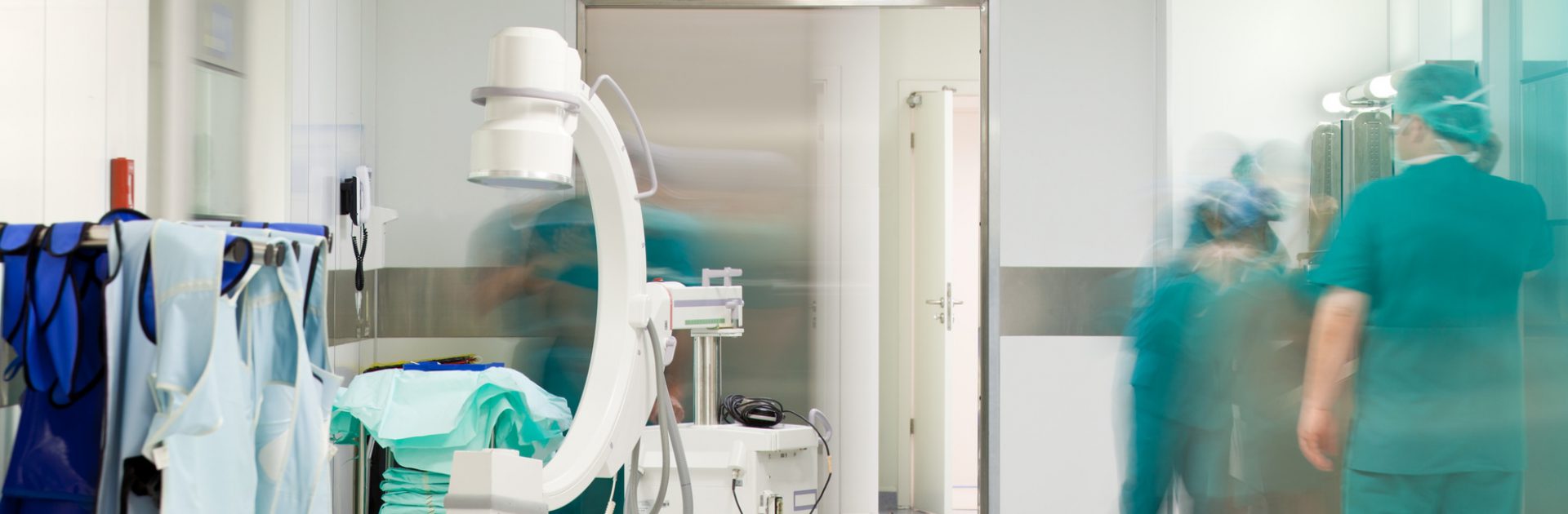 Mobile X-Ray machine in hospital corridor in front of surgery, blurred doctor figures